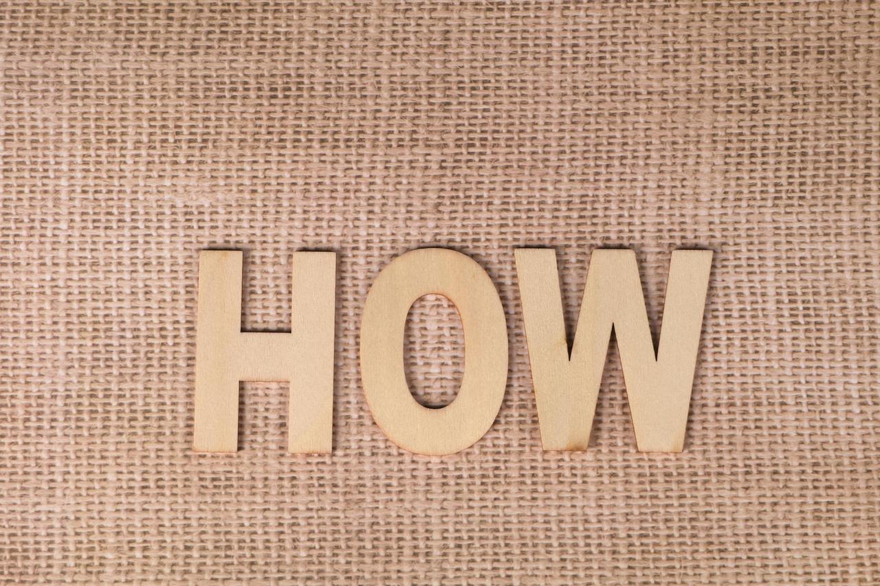 Word 'HOW' formed with wooden letters on textured burlap surface.