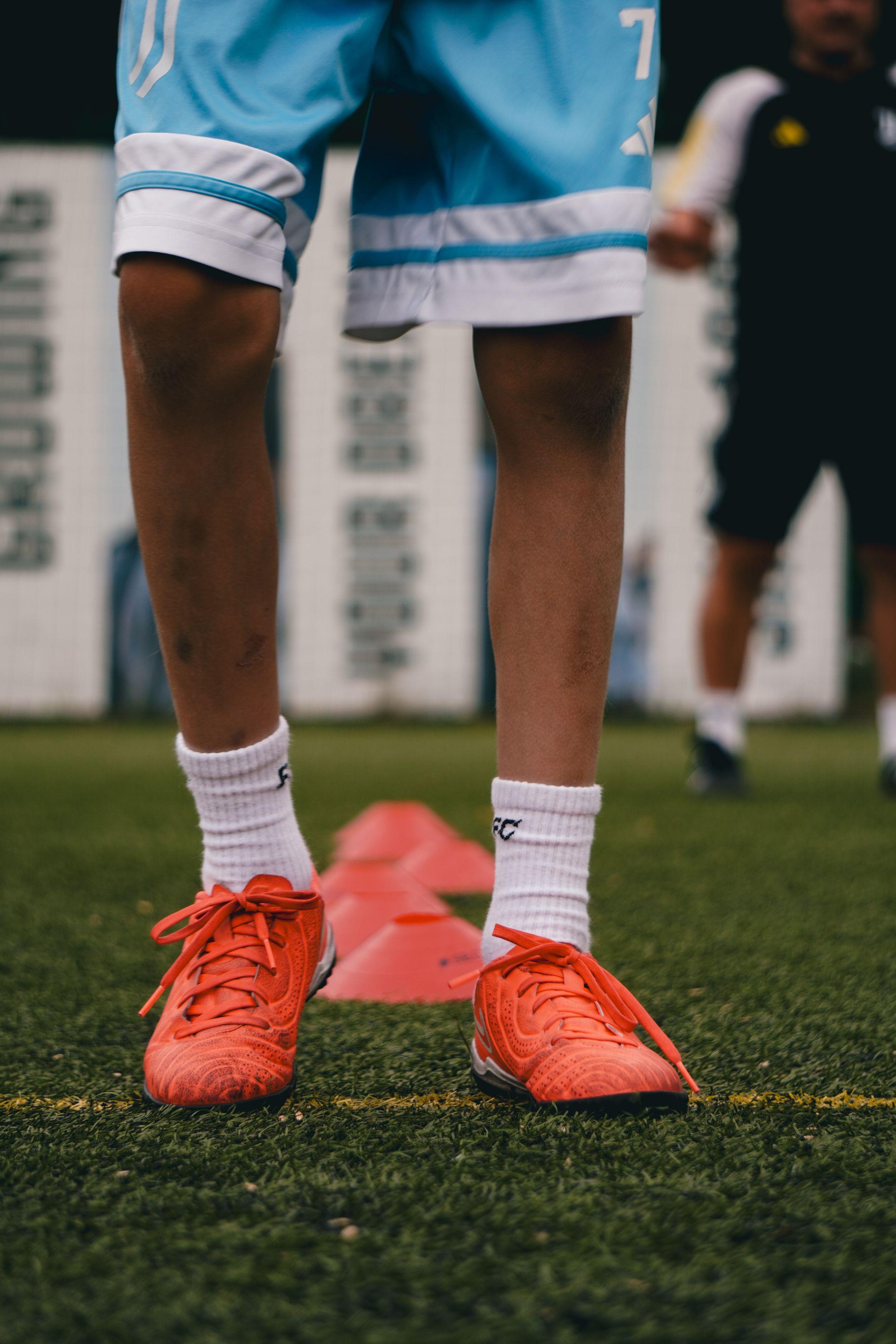 Young soccer player in training, wearing bright orange cleats on a field in Kyiv.