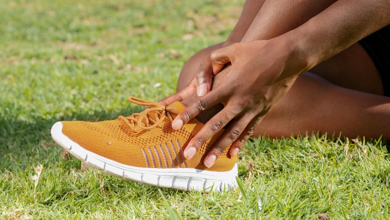 Person holding ankle in orange sneaker, suggesting potential sports injury.