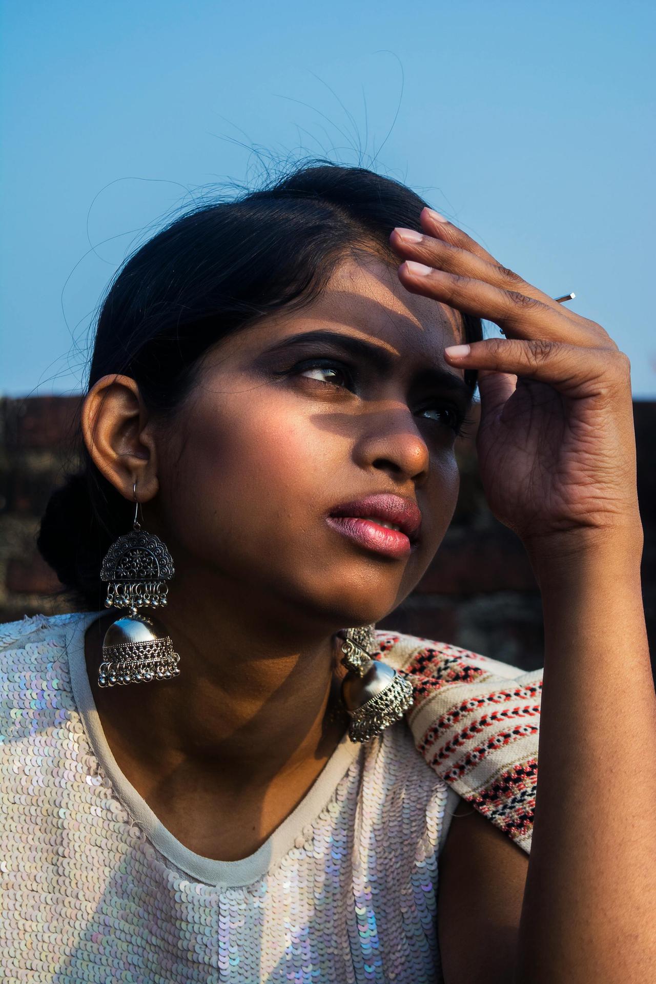 Striking portrait of a woman wearing large earrings and ethnic attire in sunlight.