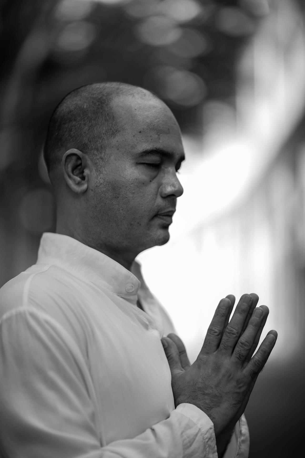 Black and white portrait of a man meditating with hands clasped outdoors.