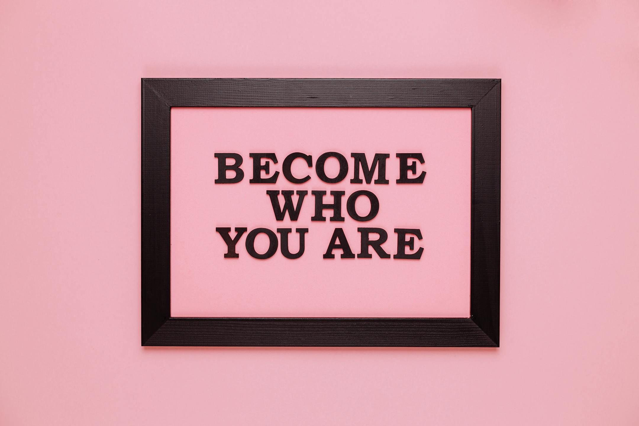 Inspiring quote 'Become Who You Are' framed on a vibrant pink wall, perfect for encouragement.
