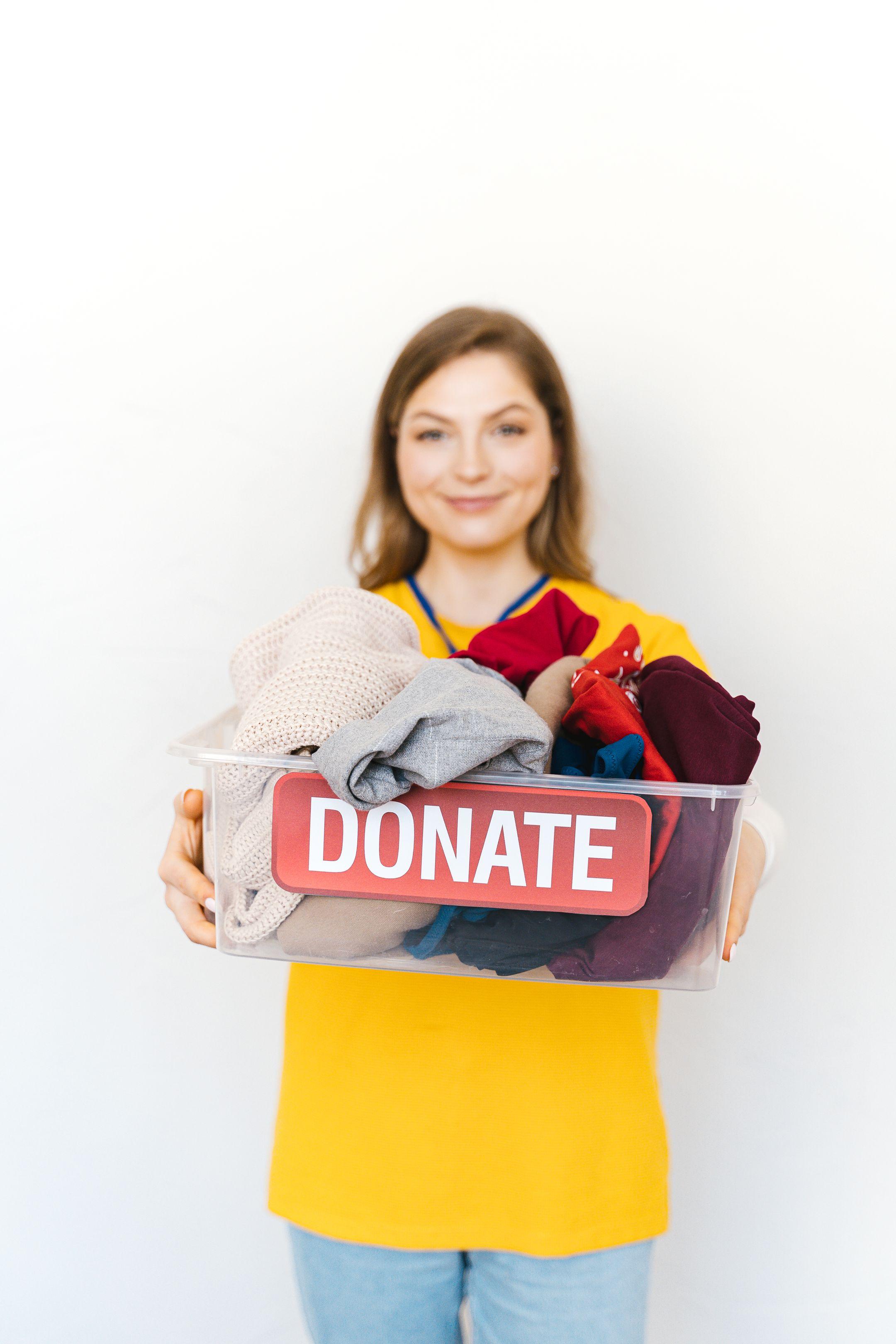 Smiling woman with clothes donation box for charity, emphasizing community support.