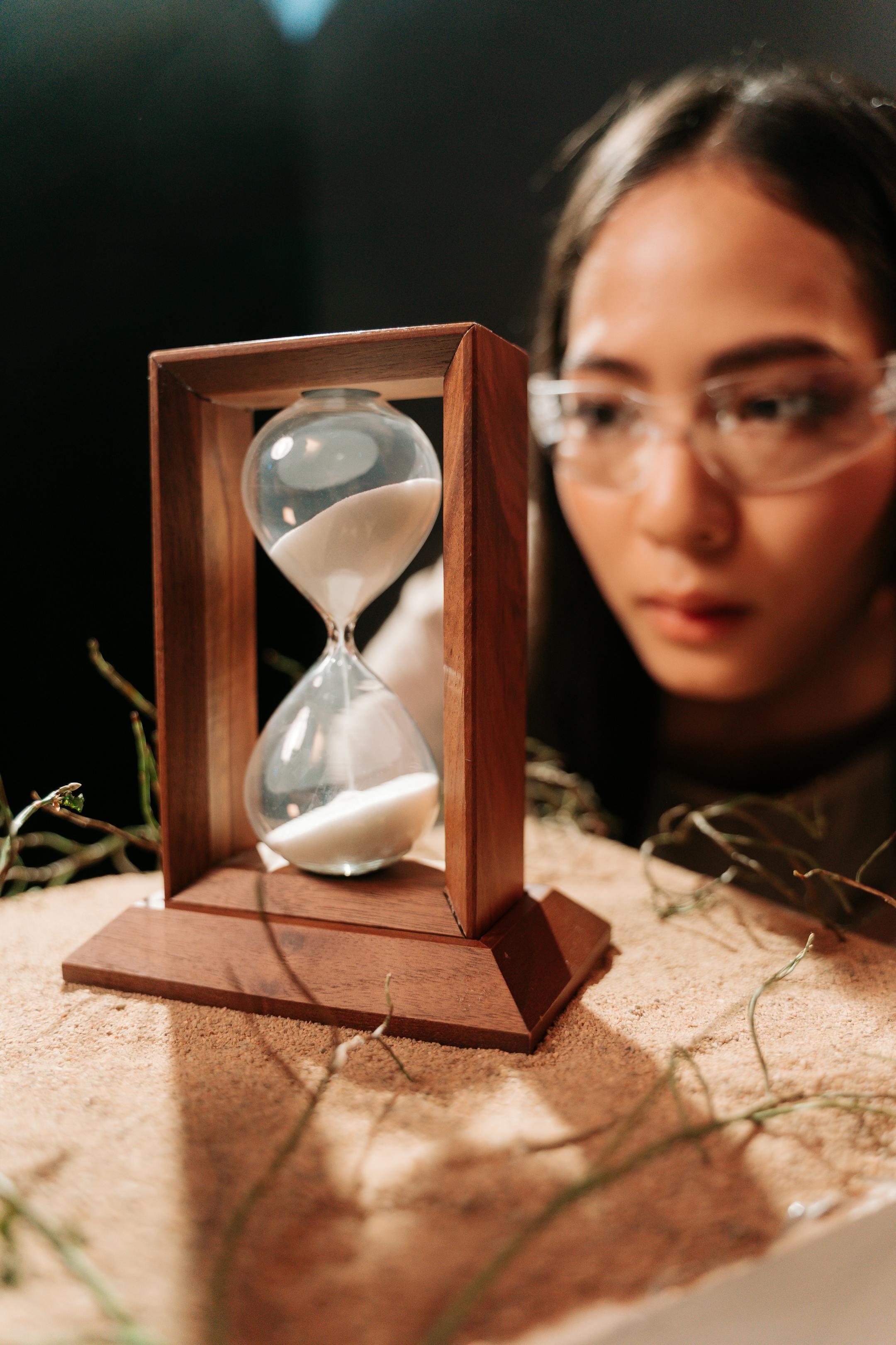 A woman attentively observing an hourglass filled with sand.