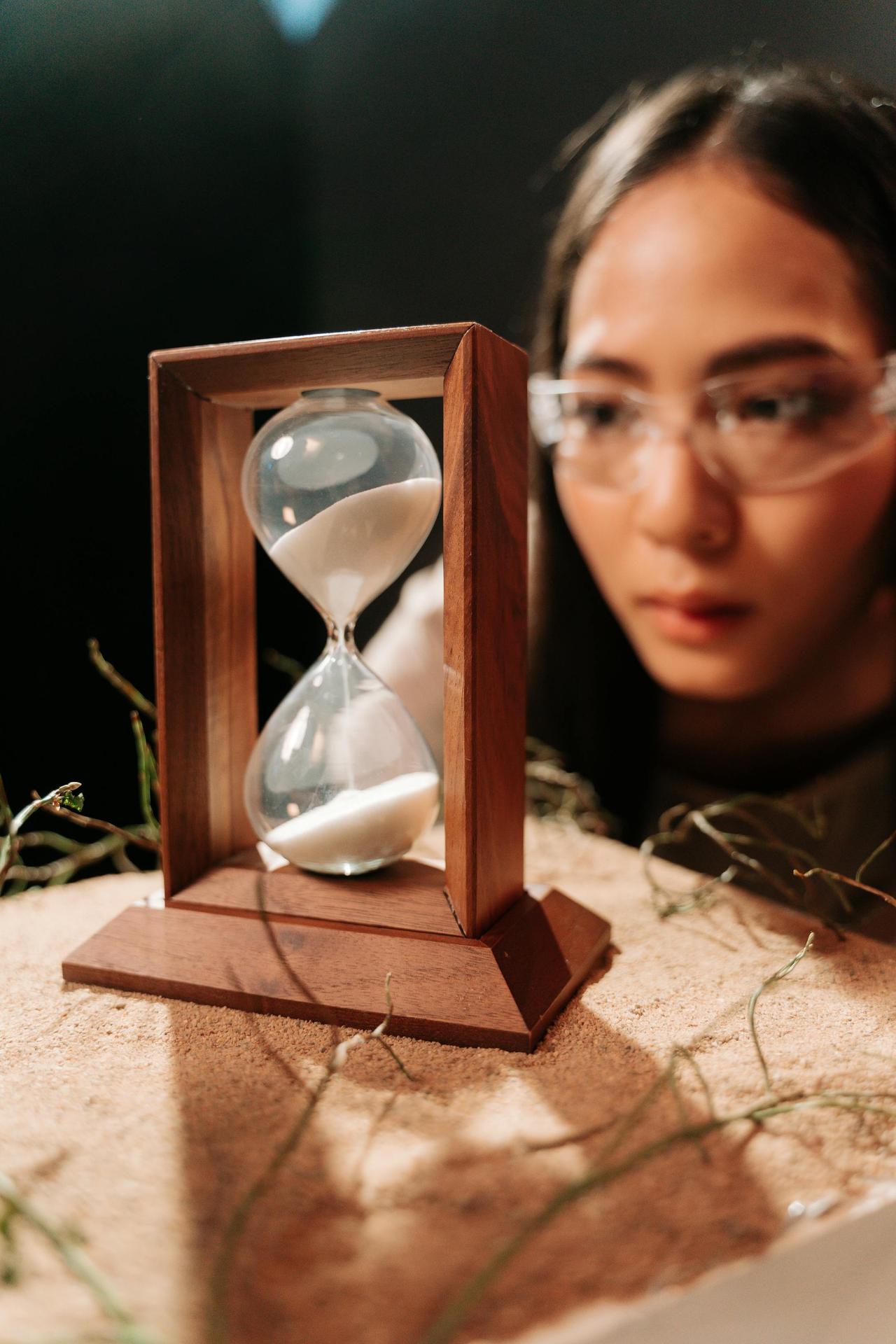 A woman attentively observing an hourglass filled with sand.