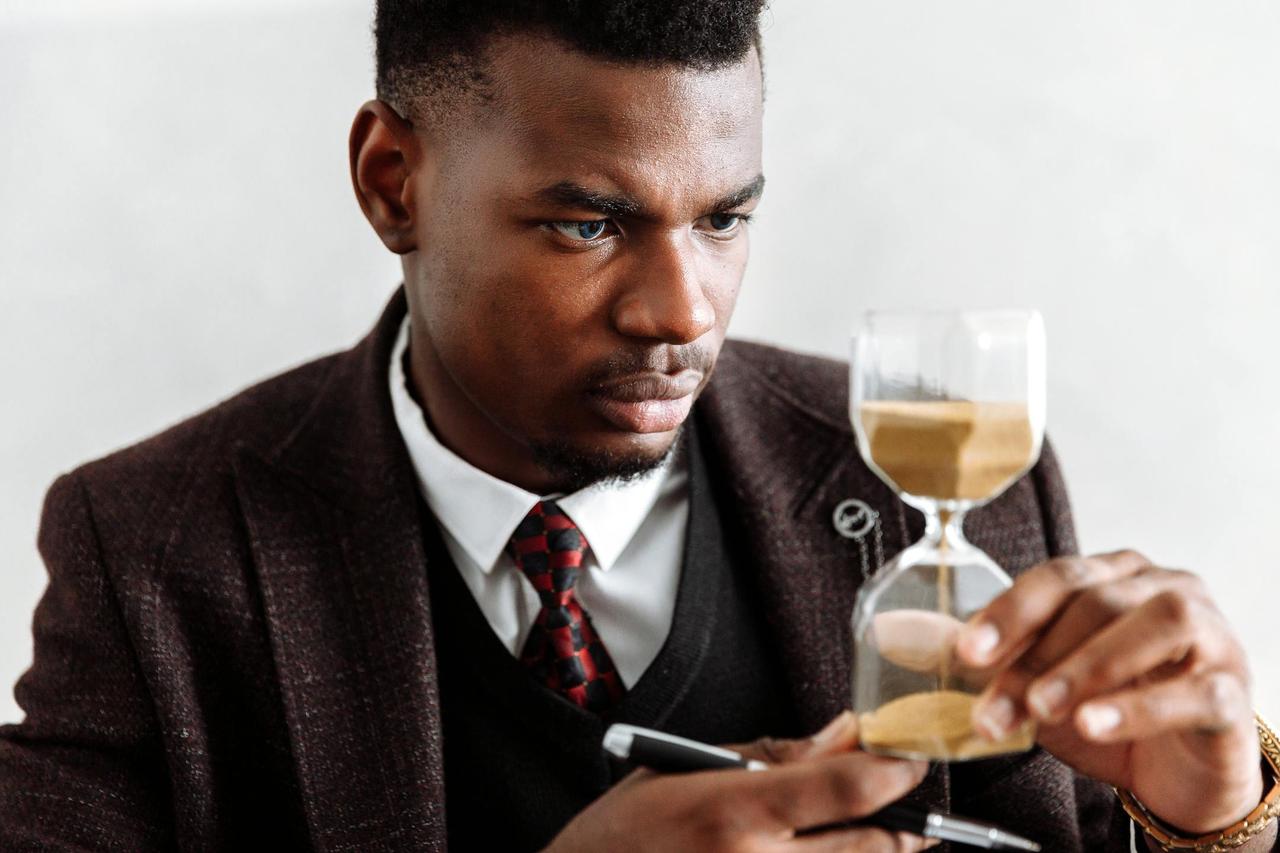 Serious businessman contemplating time with an hourglass, symbolizing focus and management.