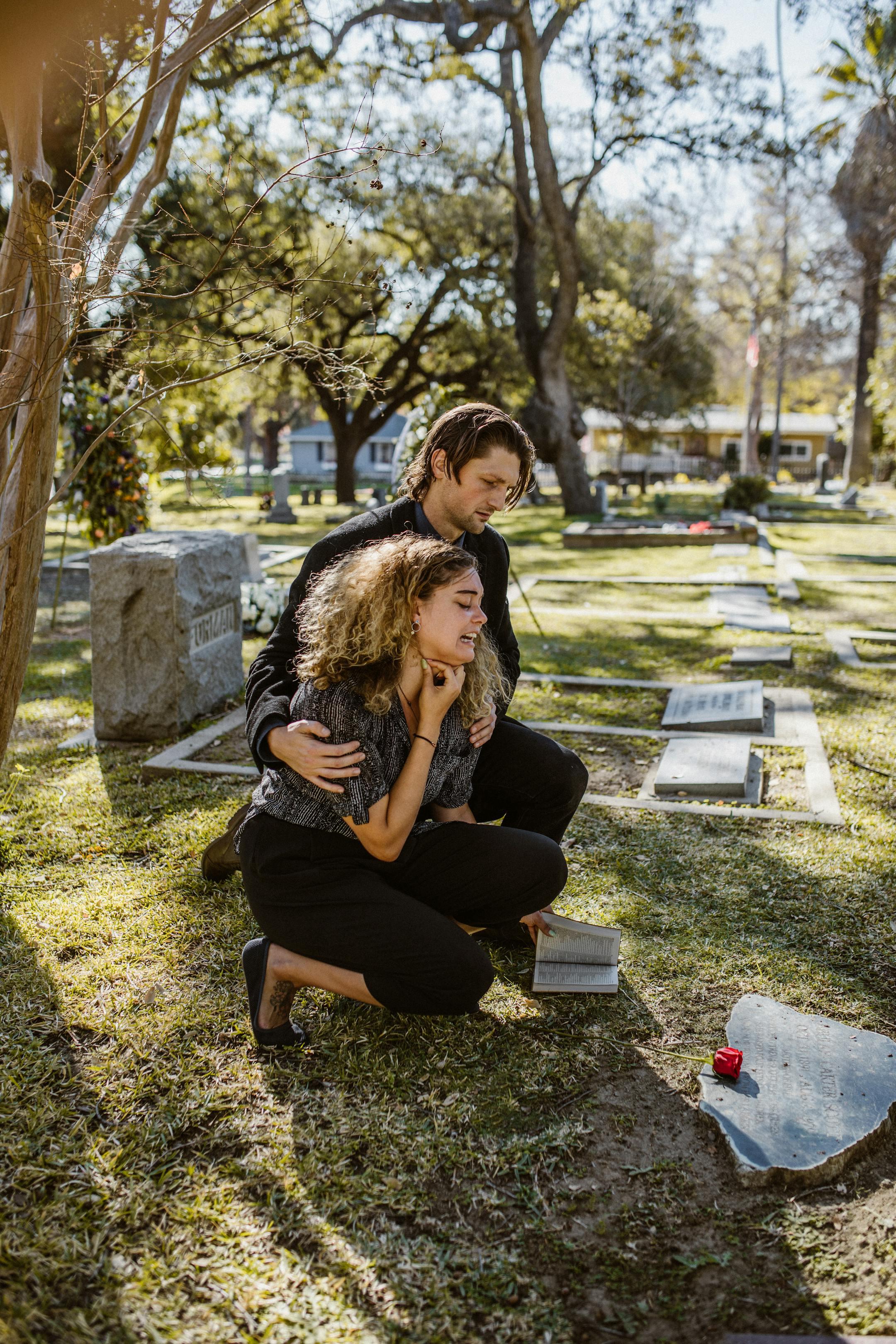 A couple mourns at a graveyard, symbolizing loss and remembrance.