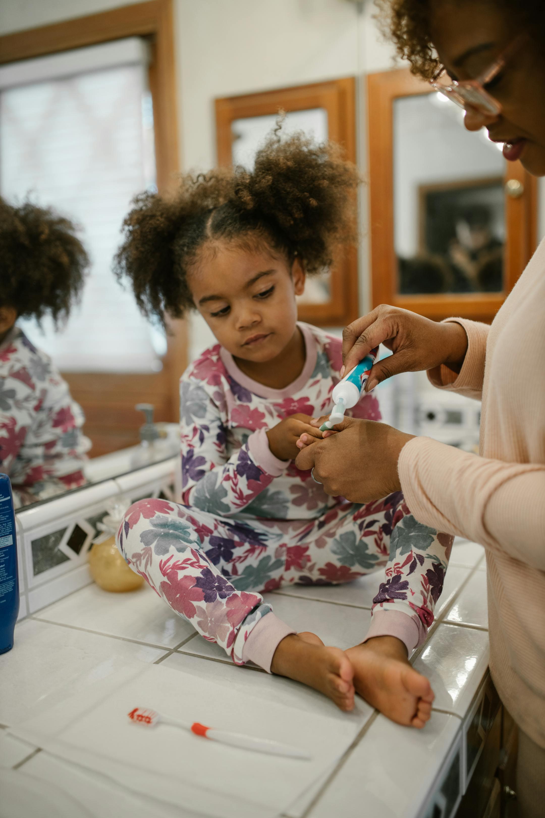 A mother assists her daughter with brushing teeth during a morning routine, fostering hygiene habits.