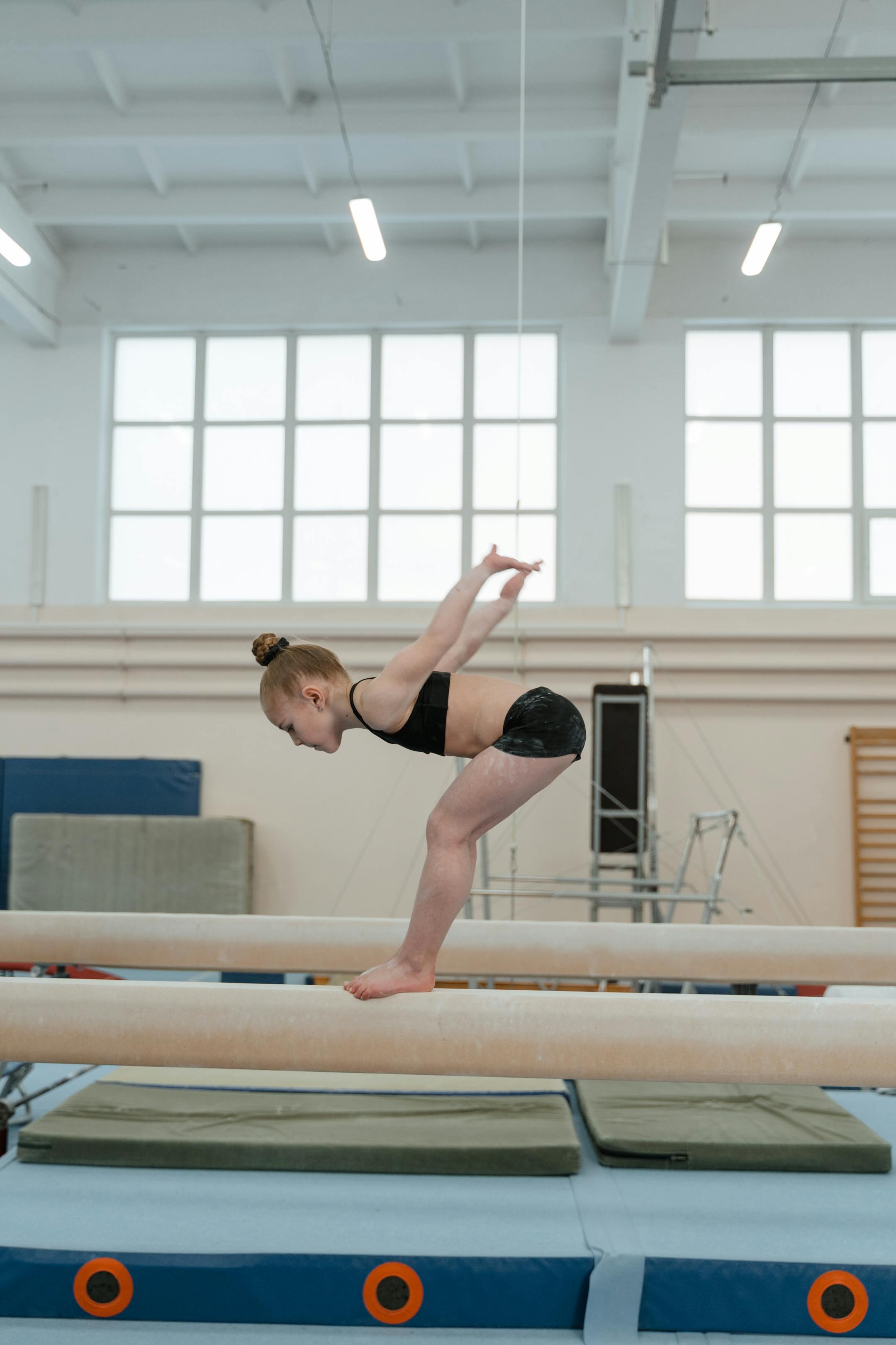 A young female gymnast practicing on a balance beam indoors, focusing on posture and poise.