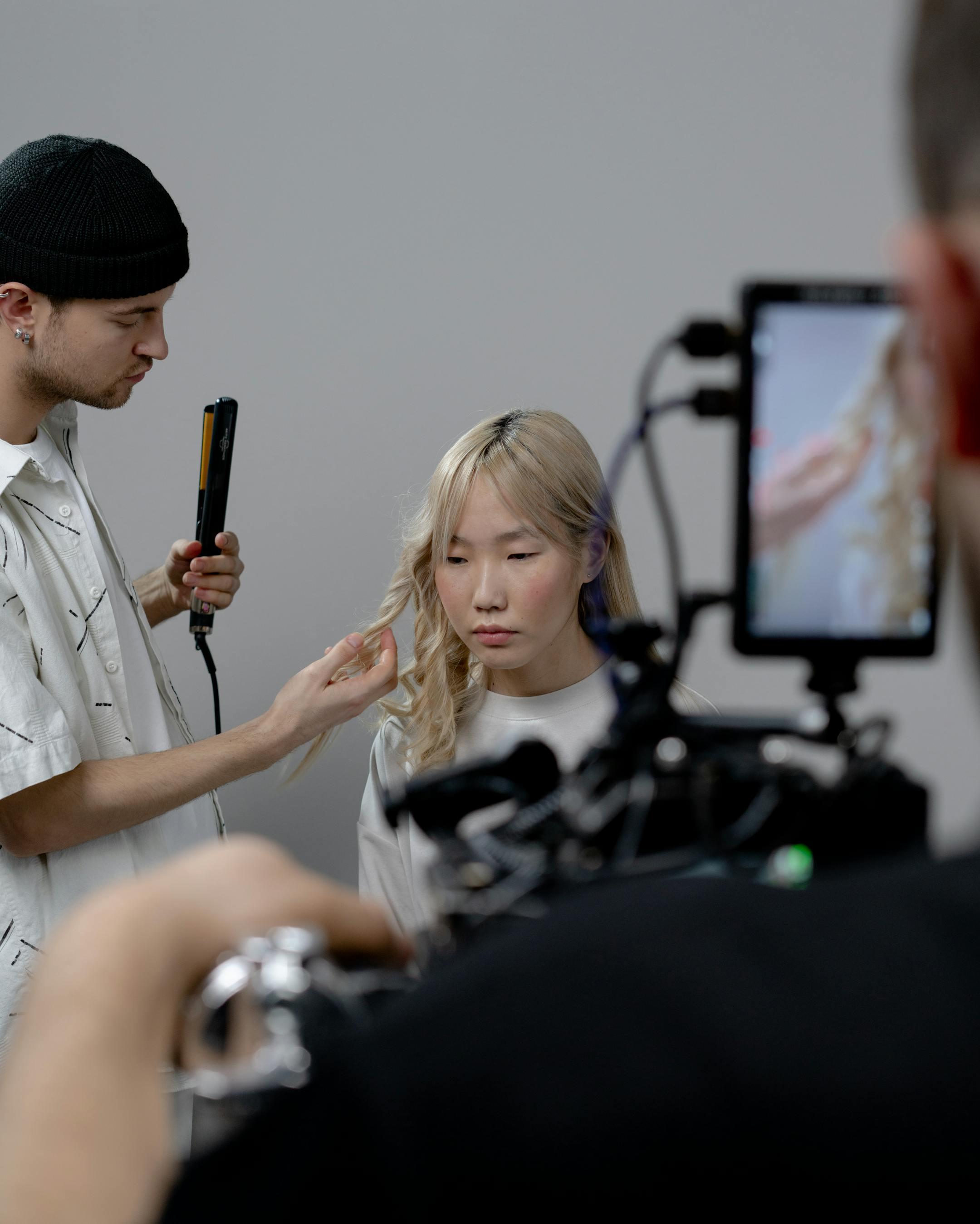 Asian woman receiving hairstyling with stylist and camera crew, studio setup.