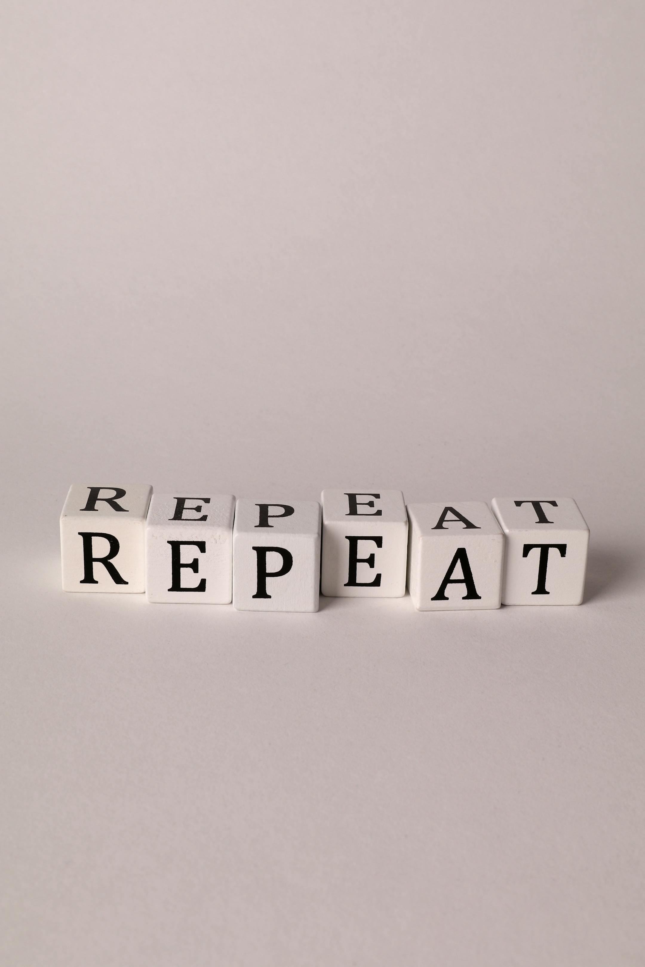 Minimalistic arrangement of white cubes spelling 'Repeat' in black letters on a neutral background.