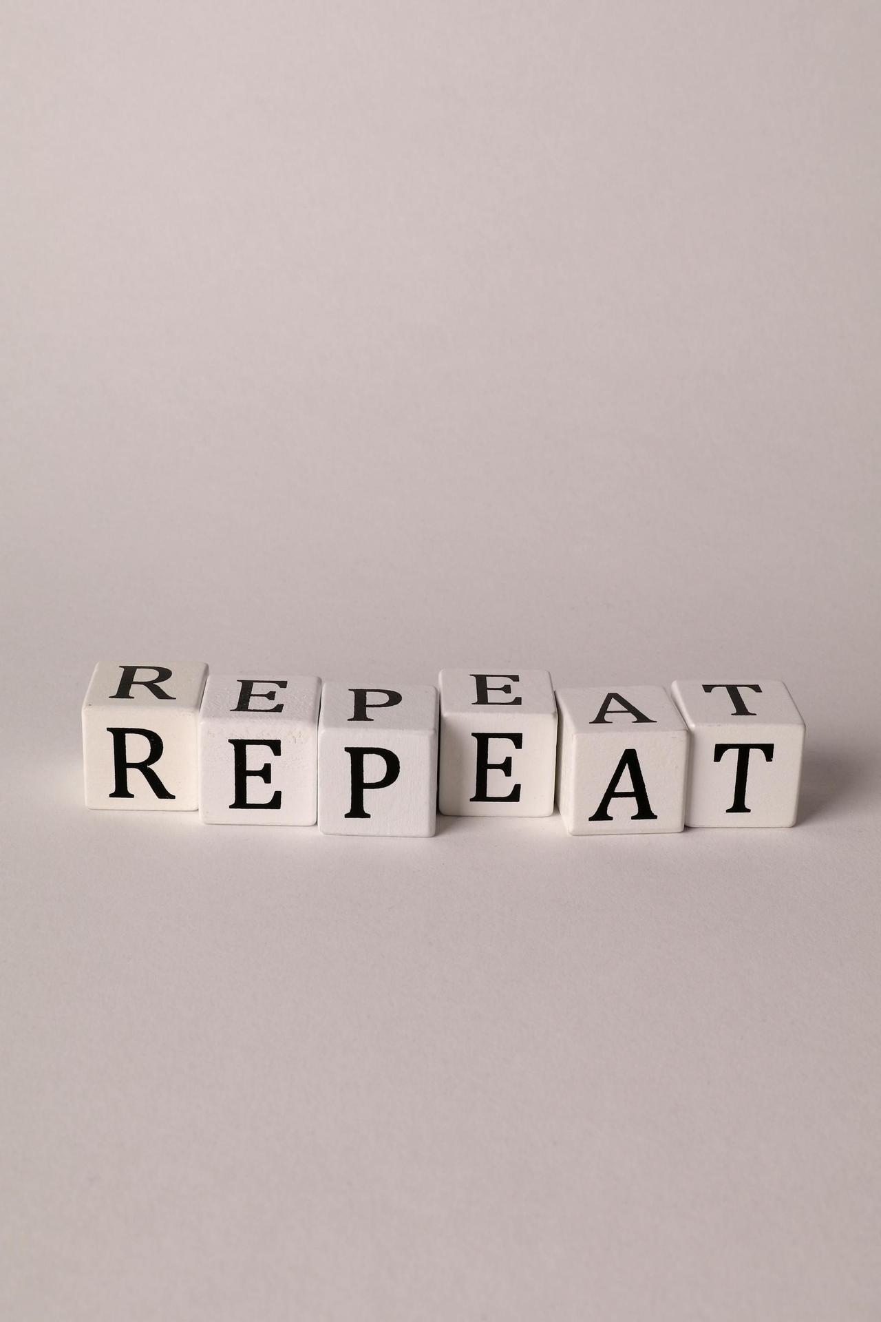 Minimalistic arrangement of white cubes spelling 'Repeat' in black letters on a neutral background.