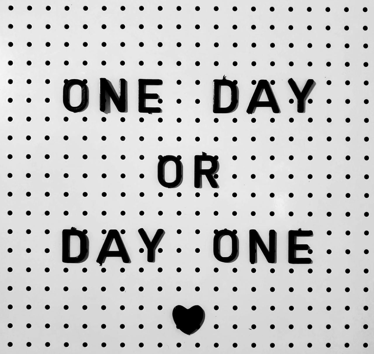 Black letters on white board saying 'One Day or Day One?' with polka dot design.