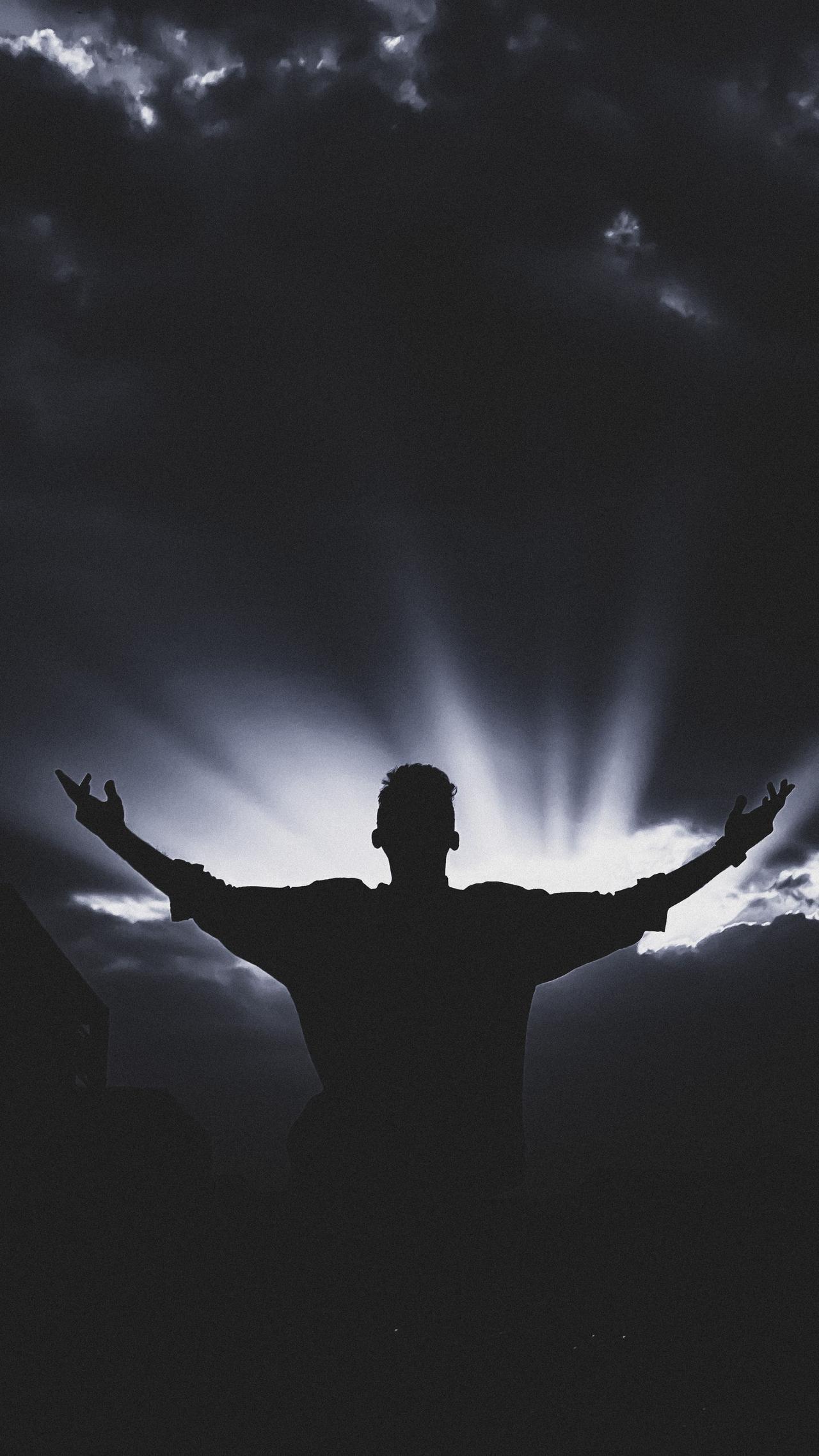 Silhouette of a man with open arms against a dramatic sunset, creating a powerful visual impact.
