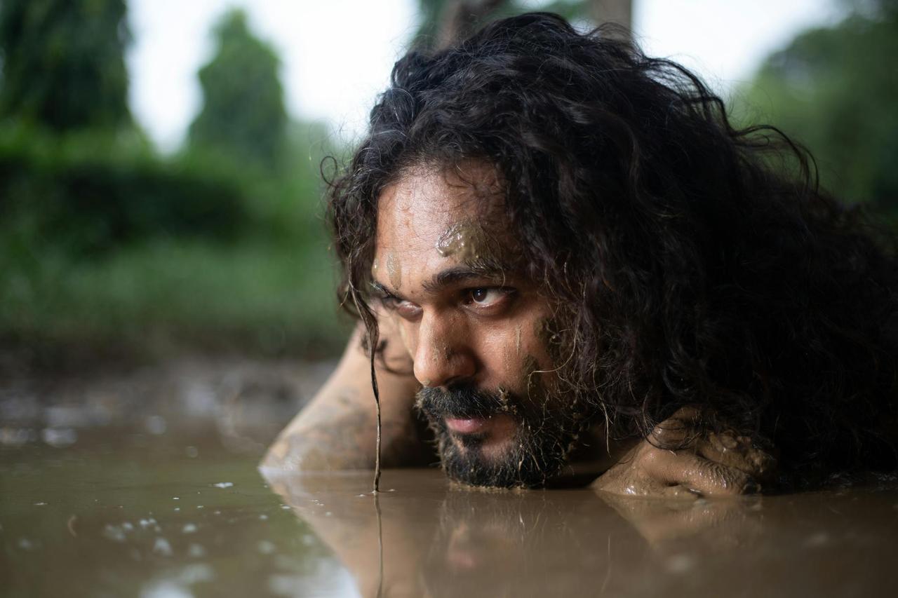 Bearded man with long hair in mud, focusing on survival and resilience.