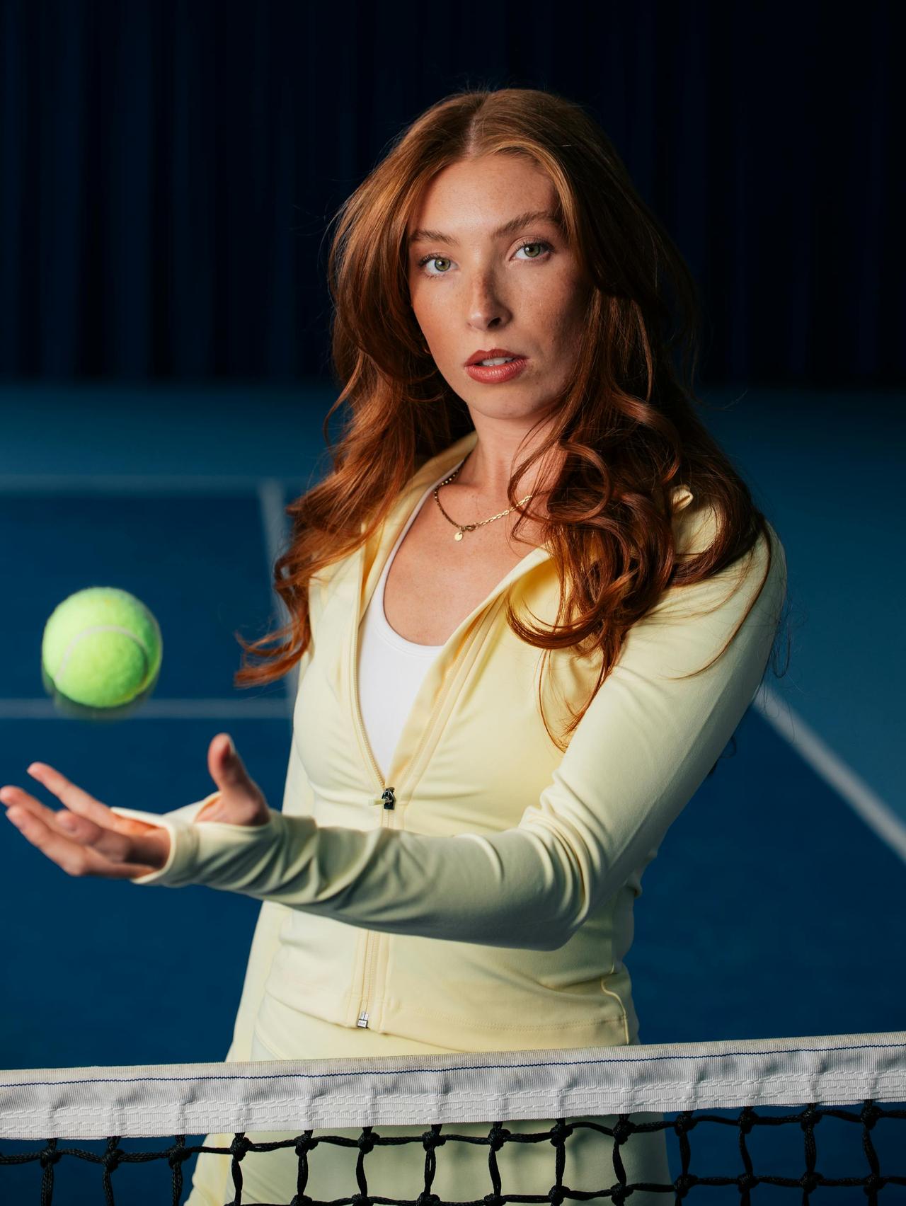 A focused female tennis player in mid-action on an indoor court, holding a tennis ball.