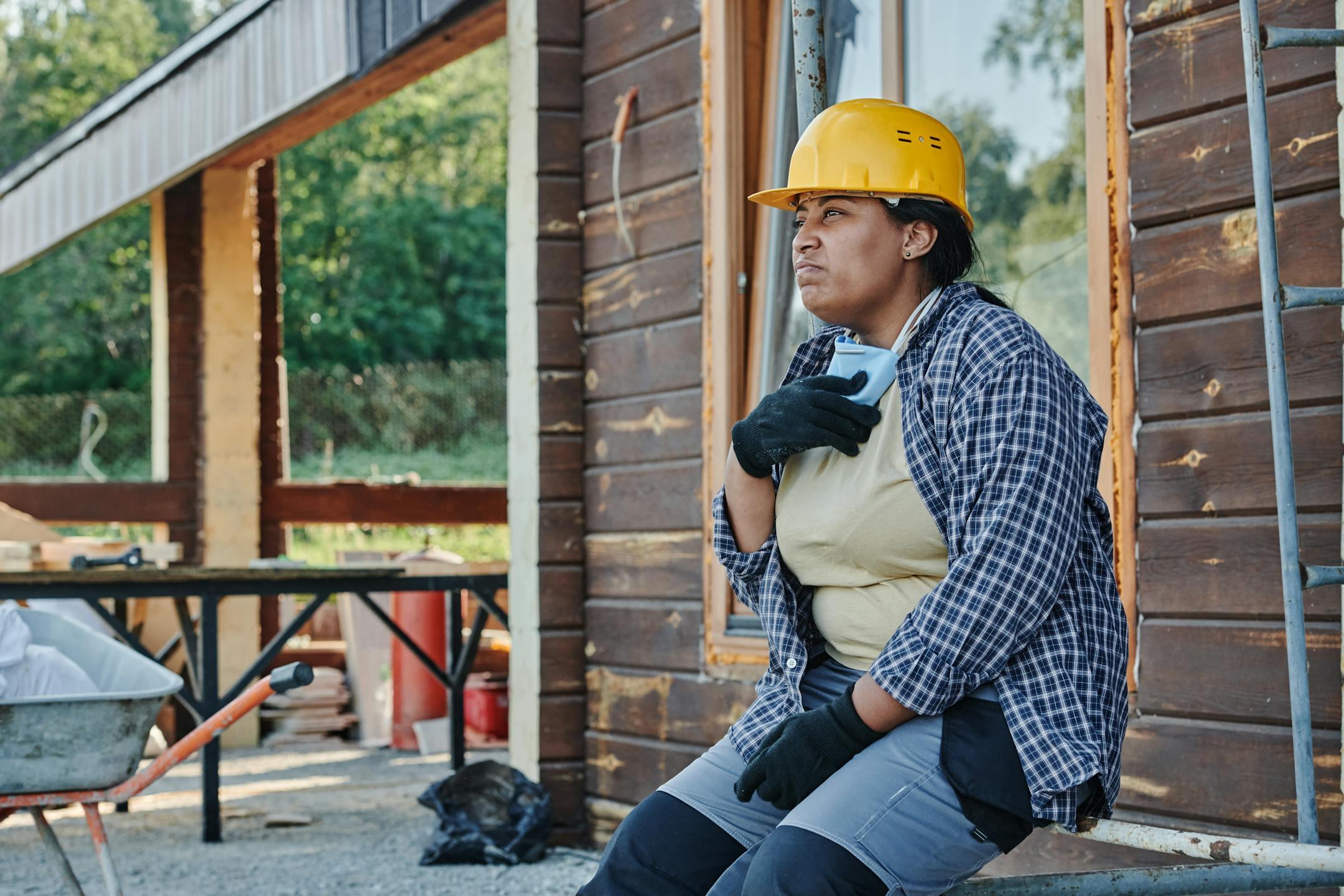 A woman construction worker in a hardhat takes a break at an outdoor site.