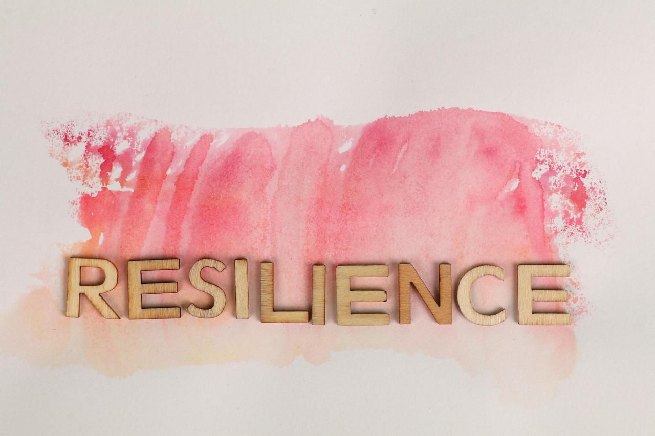 Wooden letters spelling 'resilience' on pink watercolor background, creative typography.