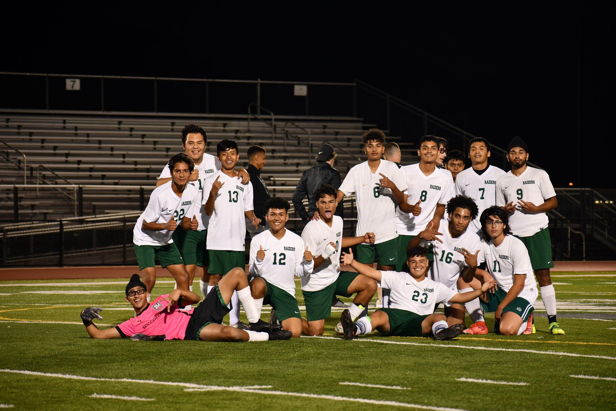 A victorious youth soccer team celebrating on the field at night in their uniforms.