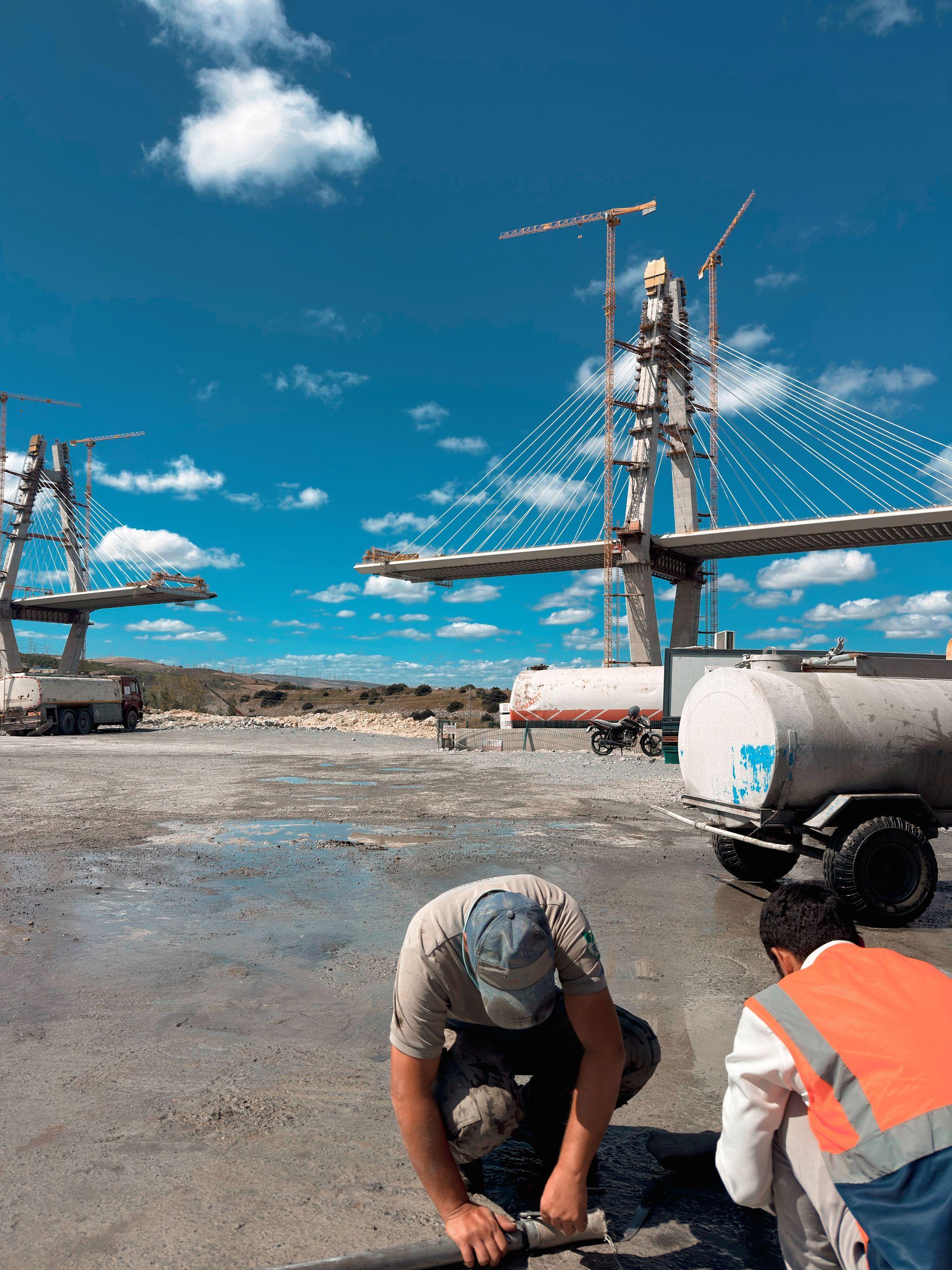 Workers prepare the site as a cable-stayed bridge is constructed under clear skies.