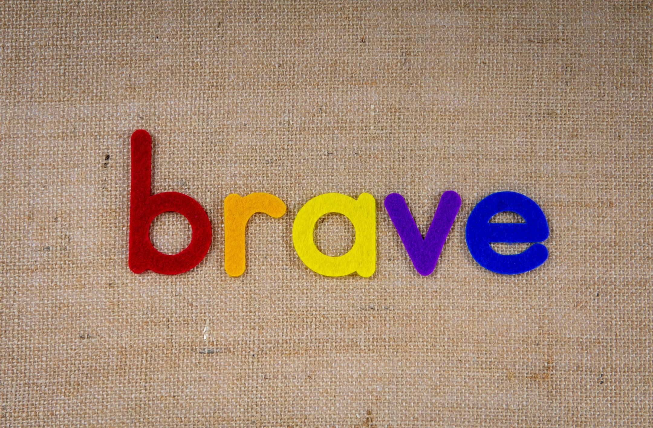 Colorful felt letters forming the word 'brave' on a burlap background.