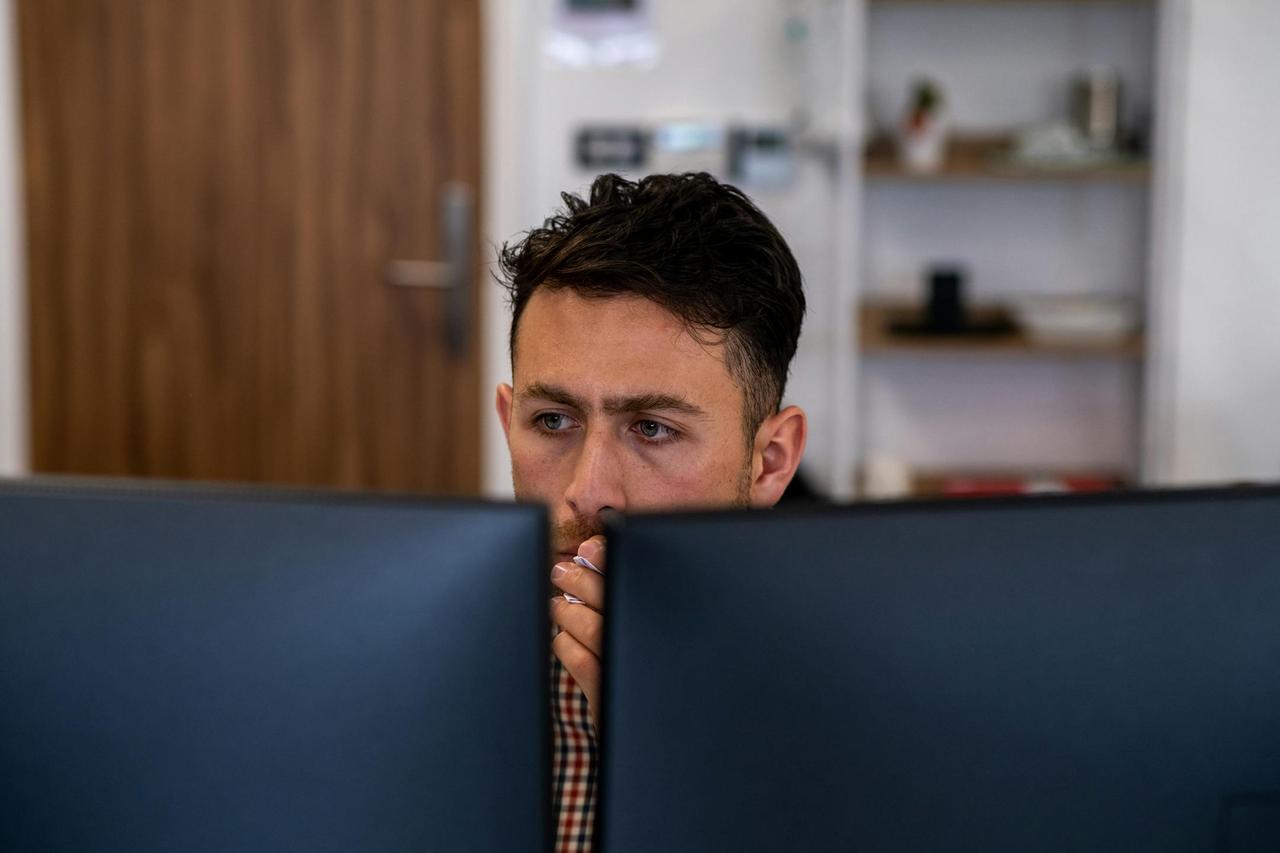 Man deeply focused on work at his office desk with dual monitors.