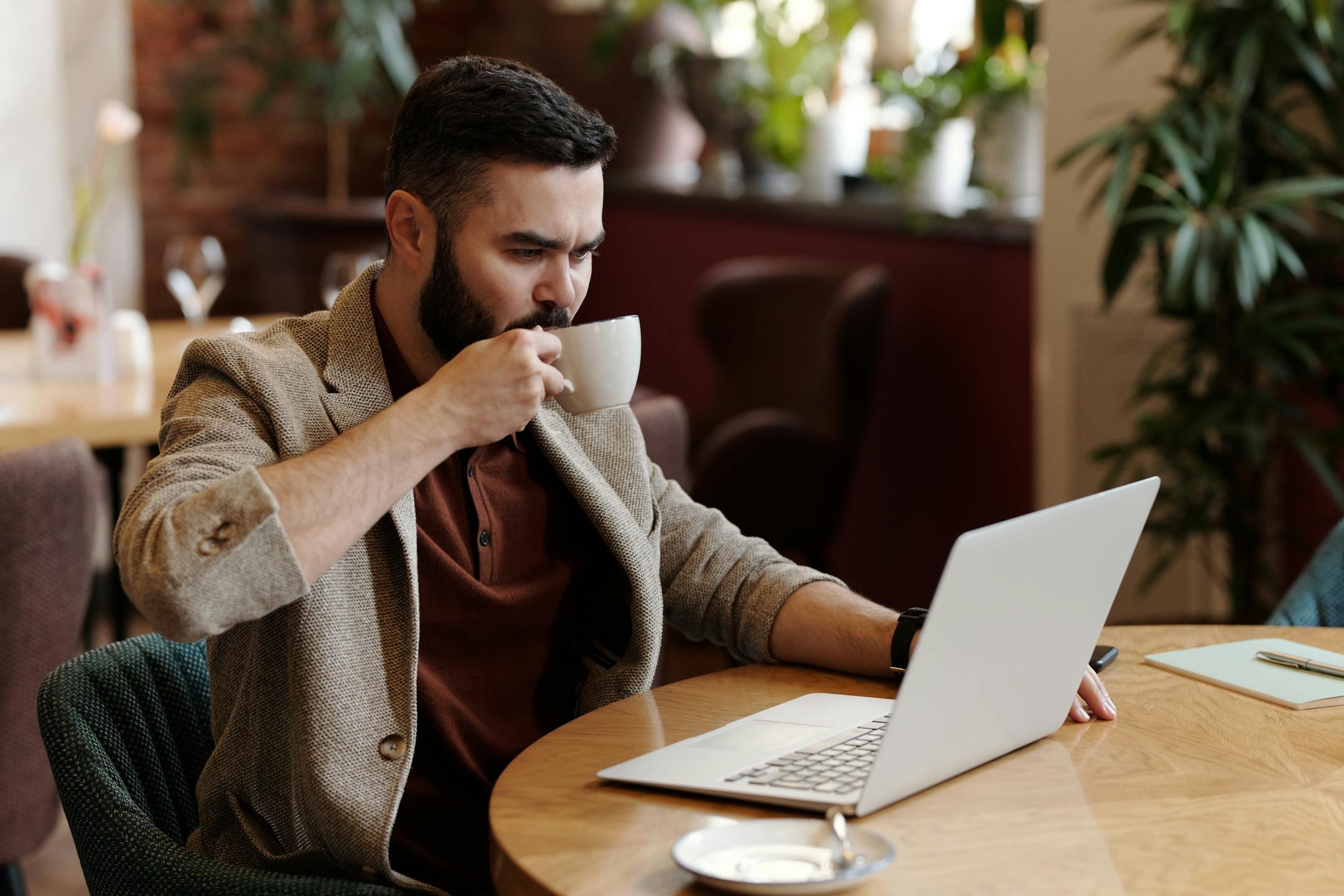 Professional man drinking coffee and working on laptop in a cozy cafe setting.