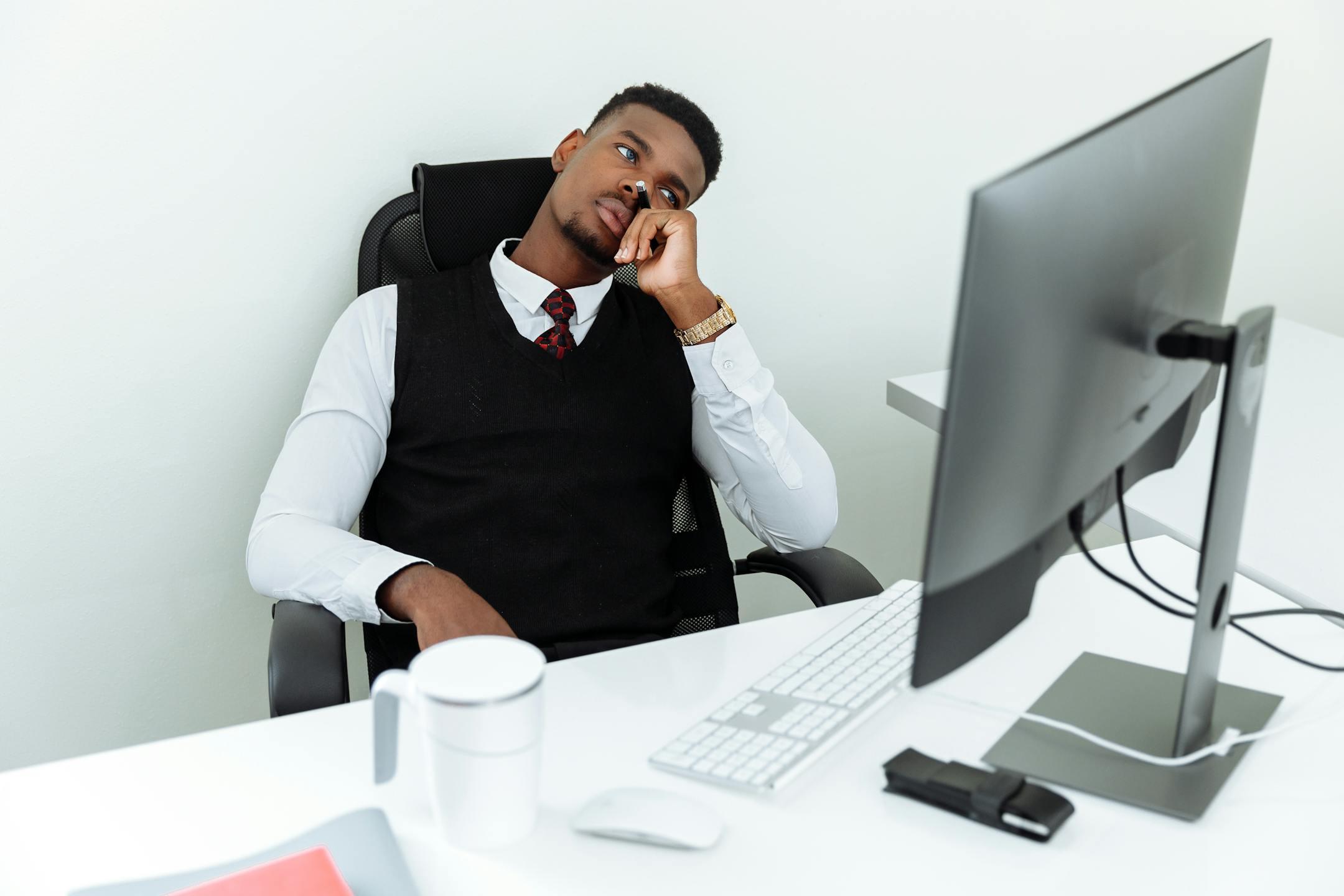 A man in business attire sits pensively at a desk with a computer, looking thoughtful.