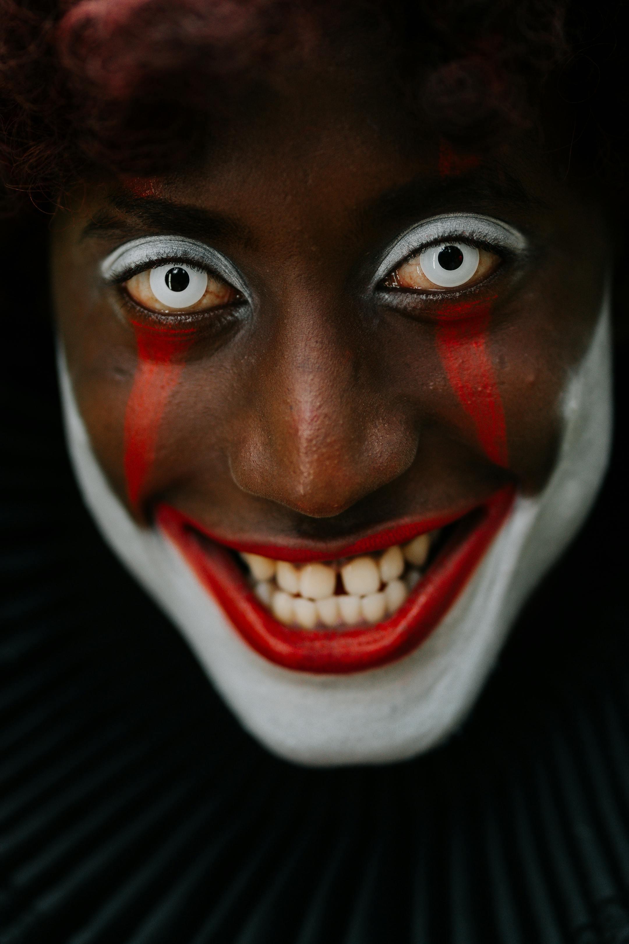 Close-up of a person in eerie clown makeup with a haunting smile and intense eyes.
