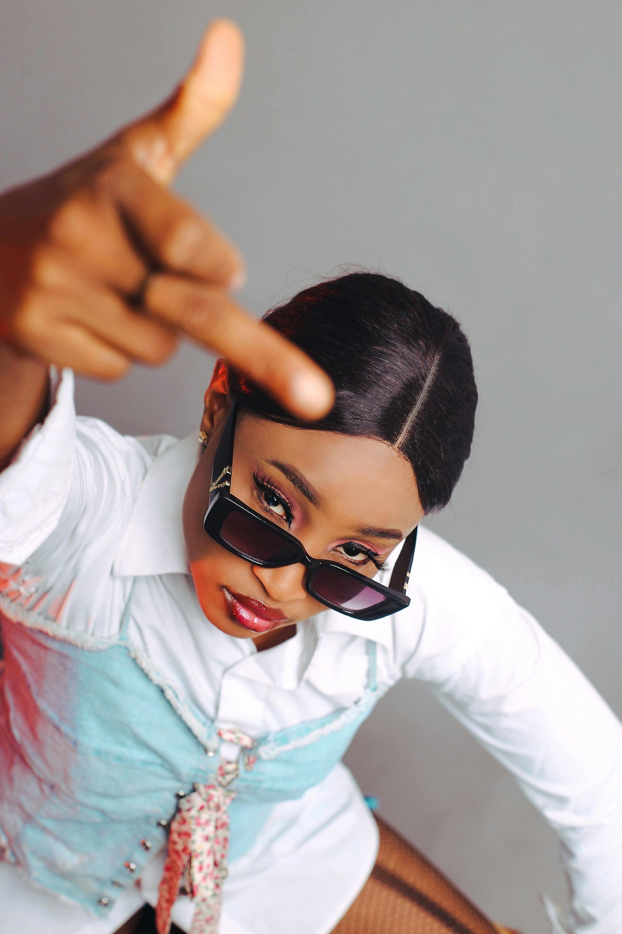 Stylish African woman making a bold gesture, wearing sunglasses indoors.