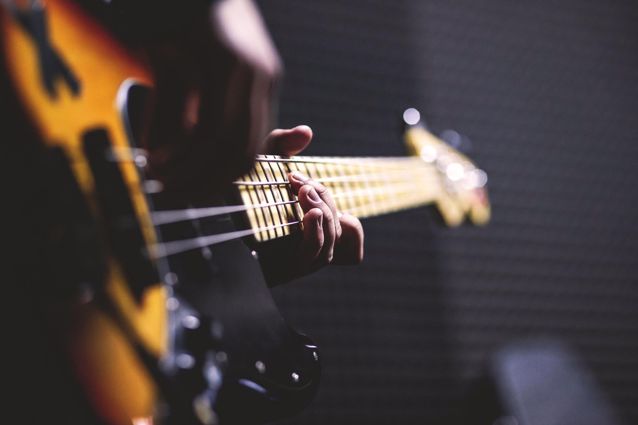 person playing sun burst electric bass guitar in bokeh